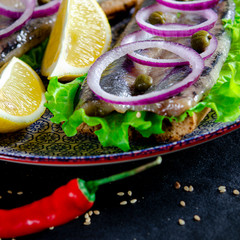 Sandwich herring on the plate, served with onions, parsley and lemon. Top view, healthy sea food.