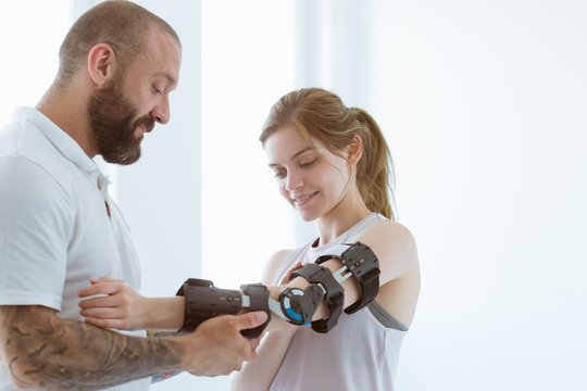 Tattooed physiotherapist who puts an orthosis on the hand of a young patient after an accident