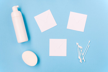 Cosmetic products on a blue background. Facial foam, soap and cotton buds. Three white sheets of paper for text. Body and skin care. Beauty salon, spa concept.