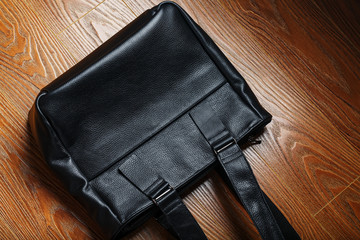 Handmade black leather bag on a wooden background, made of natural material.