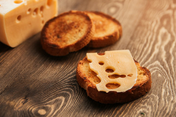 A slice of sweaty cheese and fried bread on a wooden table. Cheese with big holes. Cheese sandwich.