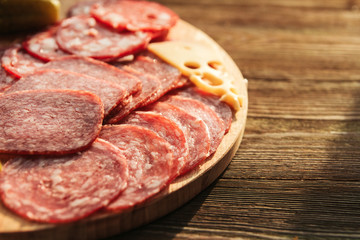 Thin slices of sausage, cheese and pickled cucumbers on a round cutting board on a wooden table. Russian appetizer.
