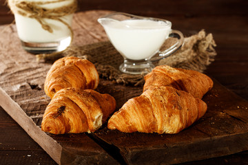 Freshly baked French croissants with cappuccino milk on a dark background with copy space.