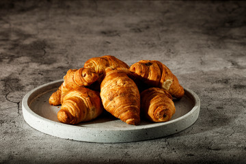 Freshly baked French croissants with cappuccino milk on a dark background with copy space.