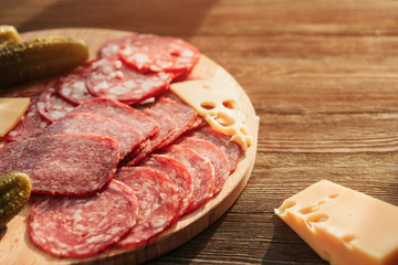 Thin slices of sausage, cheese and pickled cucumbers on a round cutting board on a wooden table. Russian appetizer.