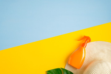 Sunblock spray bottle, beach hat and tropical leaf on blue and yellow background. Top view with copy space. Sun protection cosmetic product concept