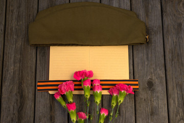 9 May holiday. Victory Day background. George ribbon, old military cap and red flowers. Symbol of 9...