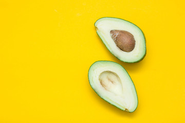 Two halves of avocado on a yellow background. Top view. Copy, empty space for text
