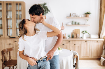 Kissing couple in their kitchen, they are dressed in white T-shirts and jeans