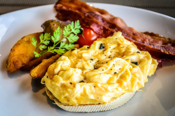 truffle egg with bacon strips and potato wedges on white plate