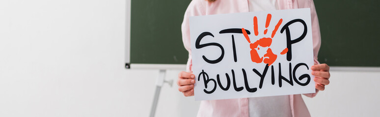 panoramic shot of schoolgirl holding placard with stop bullying lettering