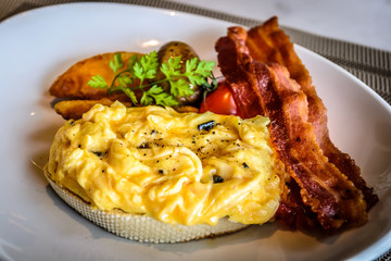 truffle egg with bacon strips and potato wedges on white plate