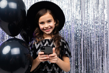 European teenage girl with a phone on her birthday on a background of black helium balloons and...