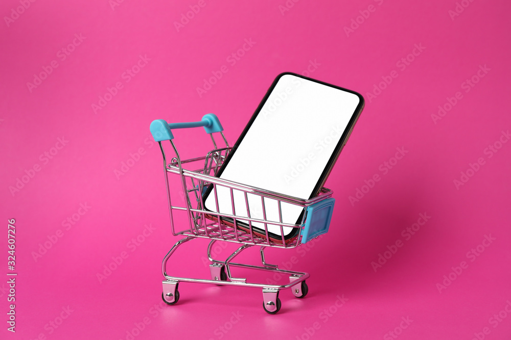 Wall mural phone with empty screen and shopping cart on pink background, close up