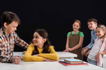 selective focus of schoolboy smiling while looking at schoolgirl near classmates isolated on black