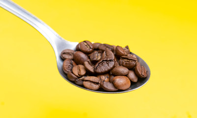 Coffee beans on a spoon with a yellow background