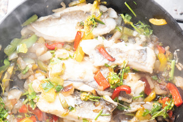 Hake with peppers and onions while being cooked in a frying pan
