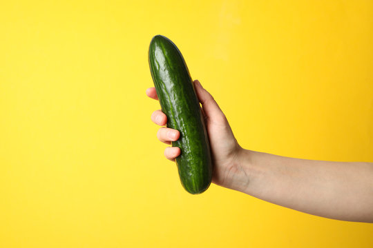Female hand holding cucumber on yellow background, space for text