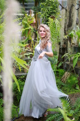 Obraz na płótnie Canvas beautiful blonde long hair girl in a flying tulle skirt walks in a botanical garden among green plants