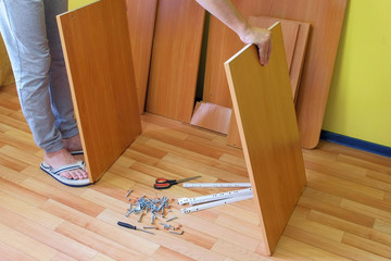 Unrecognizable man is collecting computer table in room taking parts using instructions, closeup...
