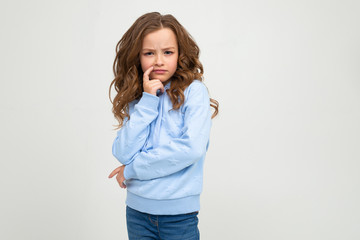 a serious teenager girl in a casual blue hoodie stands with a honest expression while holding a finger at her mouth on a white background with copy space