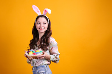 Studio portrait of young beautiful woman wearing traditional bunny ears headband for easter and smiling. Brunette female with wavy hair over yellow background. Close up, copy space.