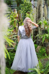 beautiful blonde long hair girl in a flying tulle skirt walks in a botanical garden among green...