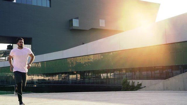 Determined young man running in slow motion while training outdoors in urban area. Individual success,movement to goal,sport lifestyle, self-confidence.3O years old sportsman jogging in city at sunset