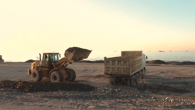 Excavator loads the excavation onto a truck (hydraulic)are heavy construction equipment consisting of an arrow,a bucket and a cabin on a rotating platform.On the beach with the sea and the setting sun