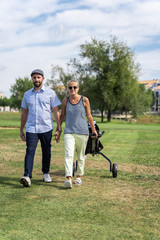 Obraz premium Couple walking hand in hand on a golf course with a cart in the summer