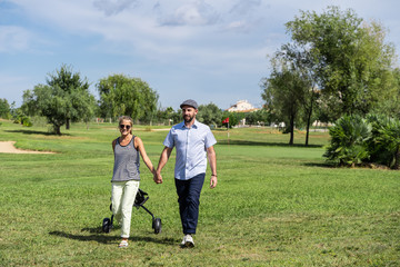 Couple walking holding hands on a golf course with a cart