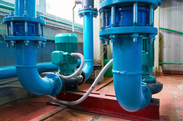 Green vertical motors with pumps on a blue colored water pipeline.
