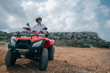 A man sits on a quad in a helmet and glasses in the mountains