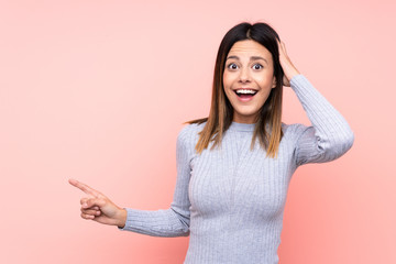 Woman over isolated pink background surprised and pointing finger to the side