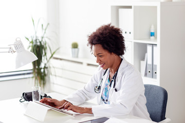 Doctor woman typing on tablet on desk in her office at hospital