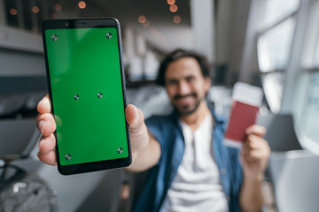 A young traveler shows on the camera a phone with a green screen.