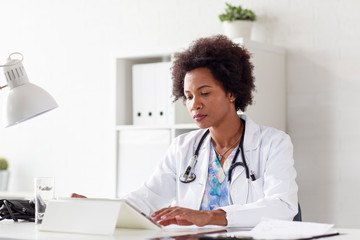 Doctor woman typing on tablet on desk in her office at hospital