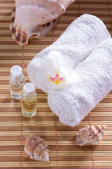 Spa setting with towel, shells, aromatic oil, orchid and candle.