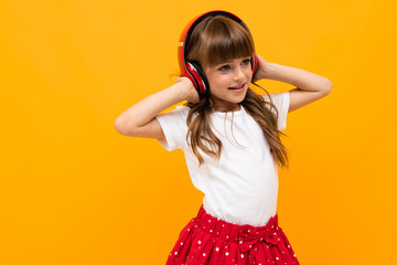 Beautiful little girl in dress listen to music isolated on yellow or orange background