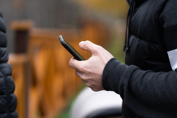 Hipster using a touch screen smart phone hands close up, vintage colors. Man using mobile smartphone - focus on top of the phone. meeting with business partners.