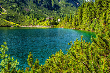 Panoramic view of the Morskie Oko mountain lake surrounding larch, pine and spruce forest with Schronisko przy Morskim Oku shelter house in background