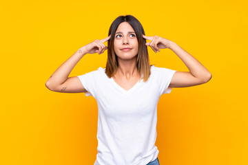 Young woman over isolated yellow background having doubts and thinking