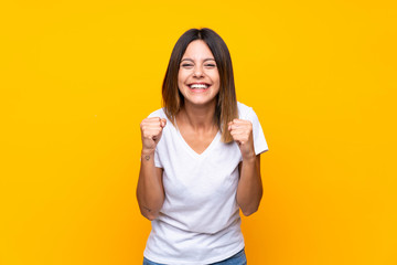 Young woman over isolated yellow background celebrating a victory in winner position