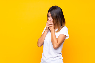 Young woman over isolated yellow background covering mouth and looking to the side