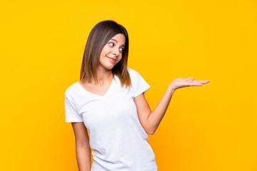 Young woman over isolated yellow background holding copyspace with doubts