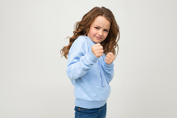 serious lady teen girl in casual blue hoodie clenched her fists in front of her on a light studio...