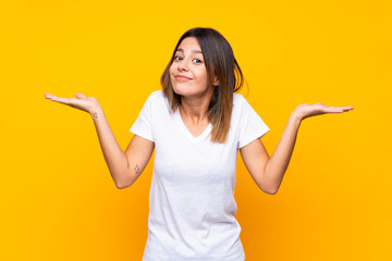Young woman over isolated yellow background making doubts gesture