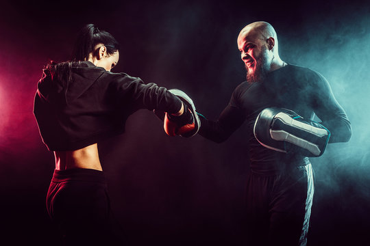Woman exercising with trainer at boxing and self defense lesson, studio, smoke on background.