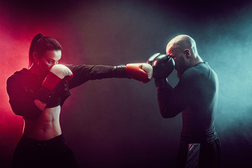 Woman exercising with trainer at boxing and self defense lesson, studio, smoke on background.