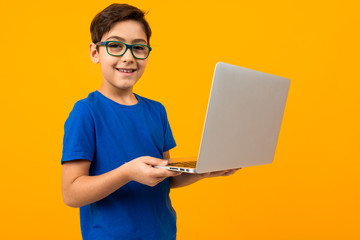 boy in blue t-shirt is typing on laptop on yellow studio background © Ivan Traimak